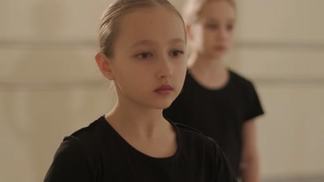 a group of young ballet students in black dancewear practicing positions in a spacious ballet studio with wooden flooring and wall-mounted barres. focused expressions and synchronized movements.