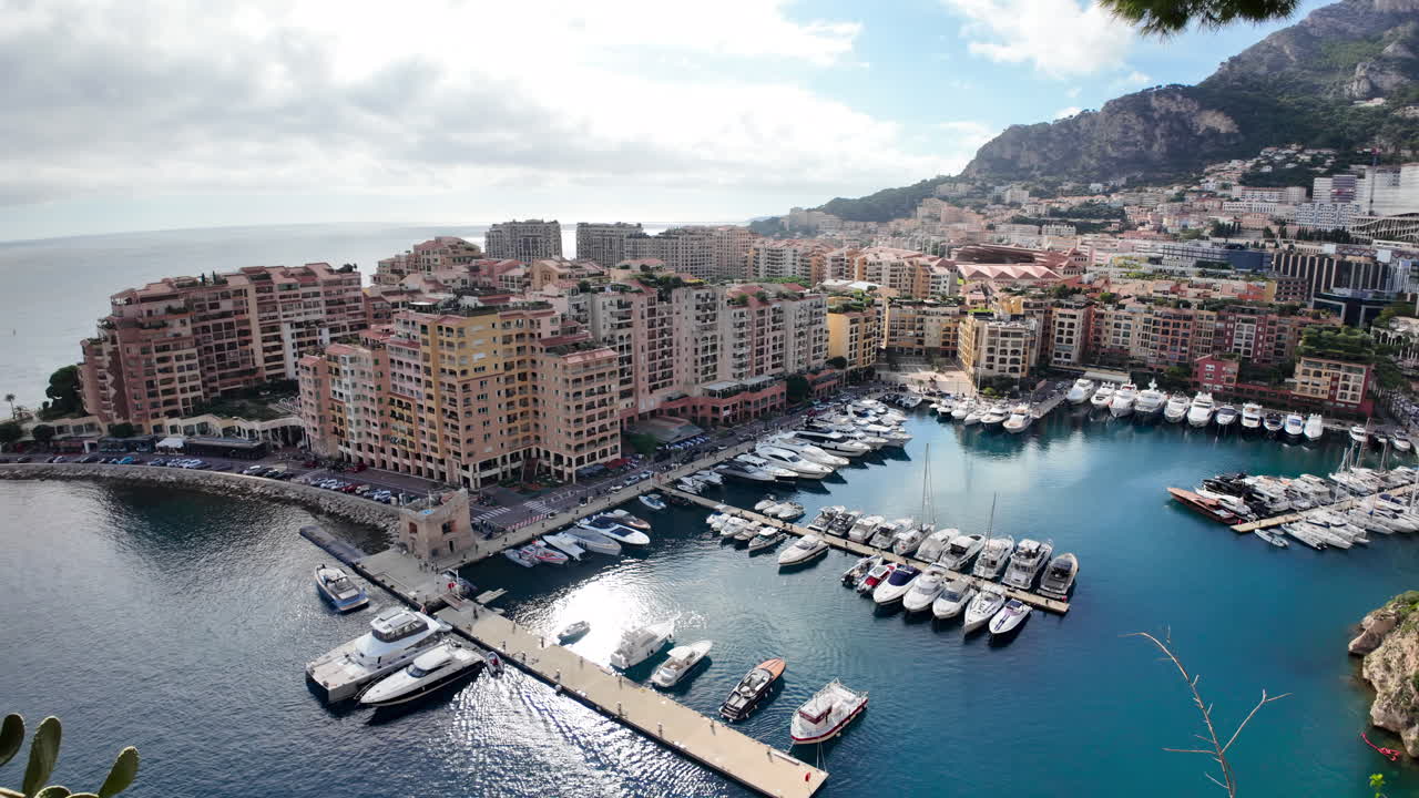 Vista dall'alto di Port de Fontvieille a Monaco, con edifici colorati, yacht di lusso e il paesaggio montuoso circostante