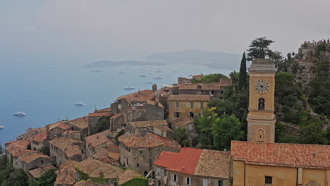 eze francia antena v23 cinemática drone de bajo nivel vuela alrededor de la aldea de la ladera con antiguos edificios medievales y la iglesia de notre dame de l&#39;assomption - julio de 2021