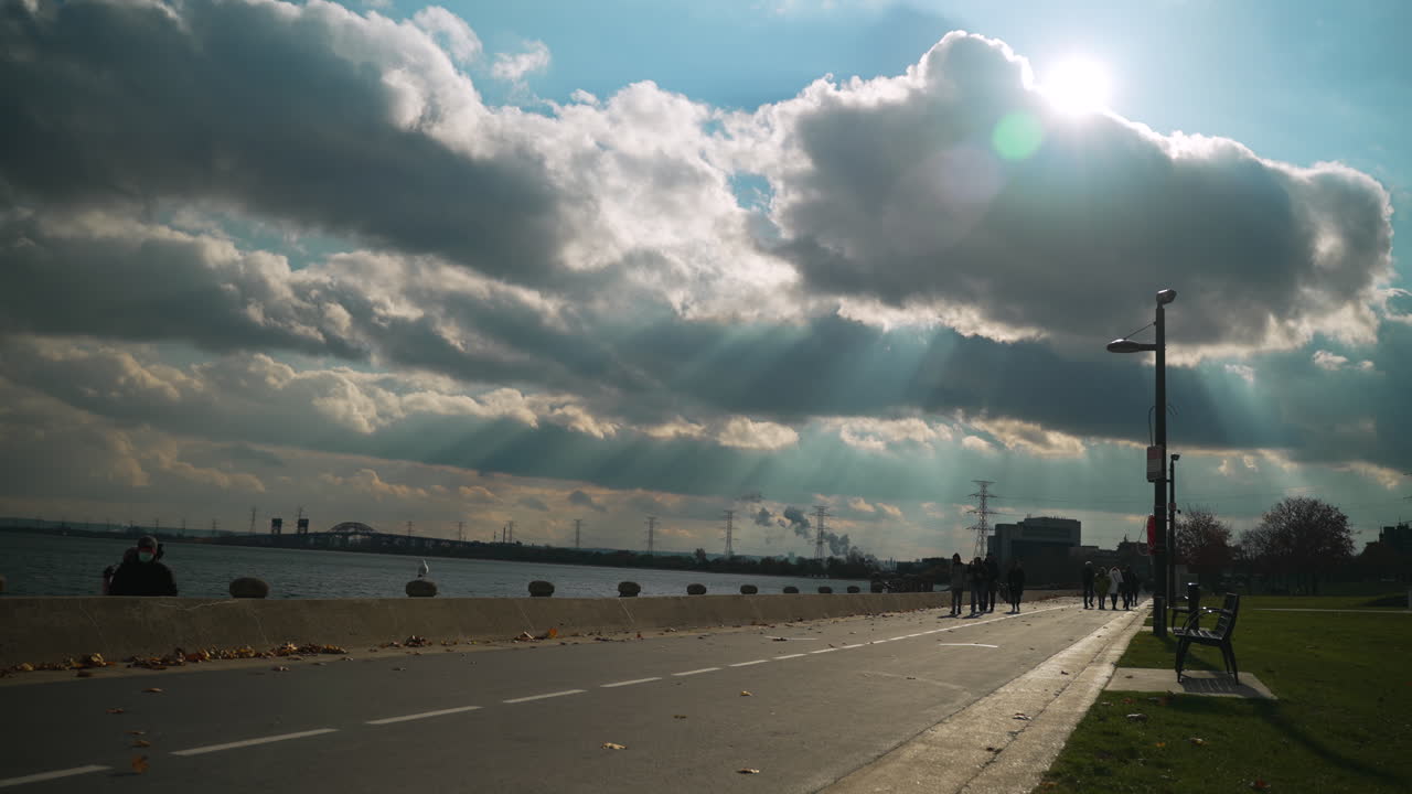 Beautiful god-rays from the sun and clouds on waterfront walkway on a beautiful summer day. Slow motion