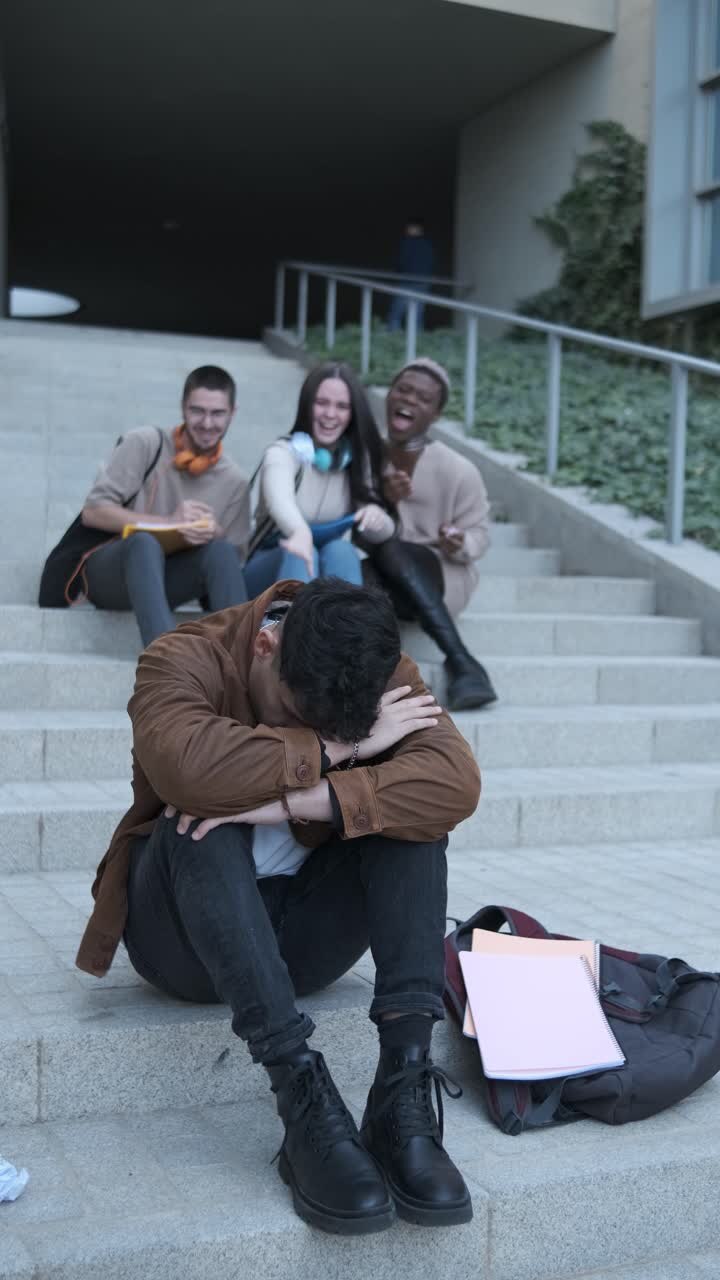 Group of students bulling a latin man sitting on the stairs outdoors