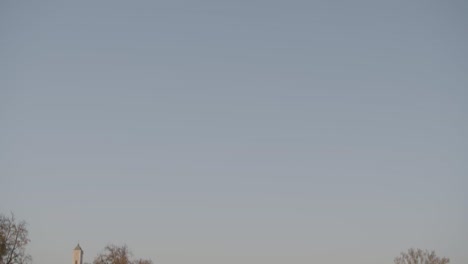 Quiet-European-village-at-dusk,-with-a-prominent-church-tower-and-houses-nestled-among-trees,-wide-shot