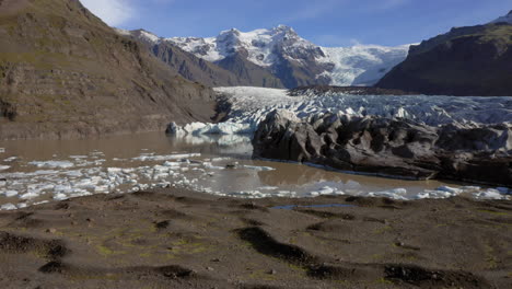 aerial: backwards reveal shot of one person standing on a hill near svinafellsjokull glacier during a sunny day