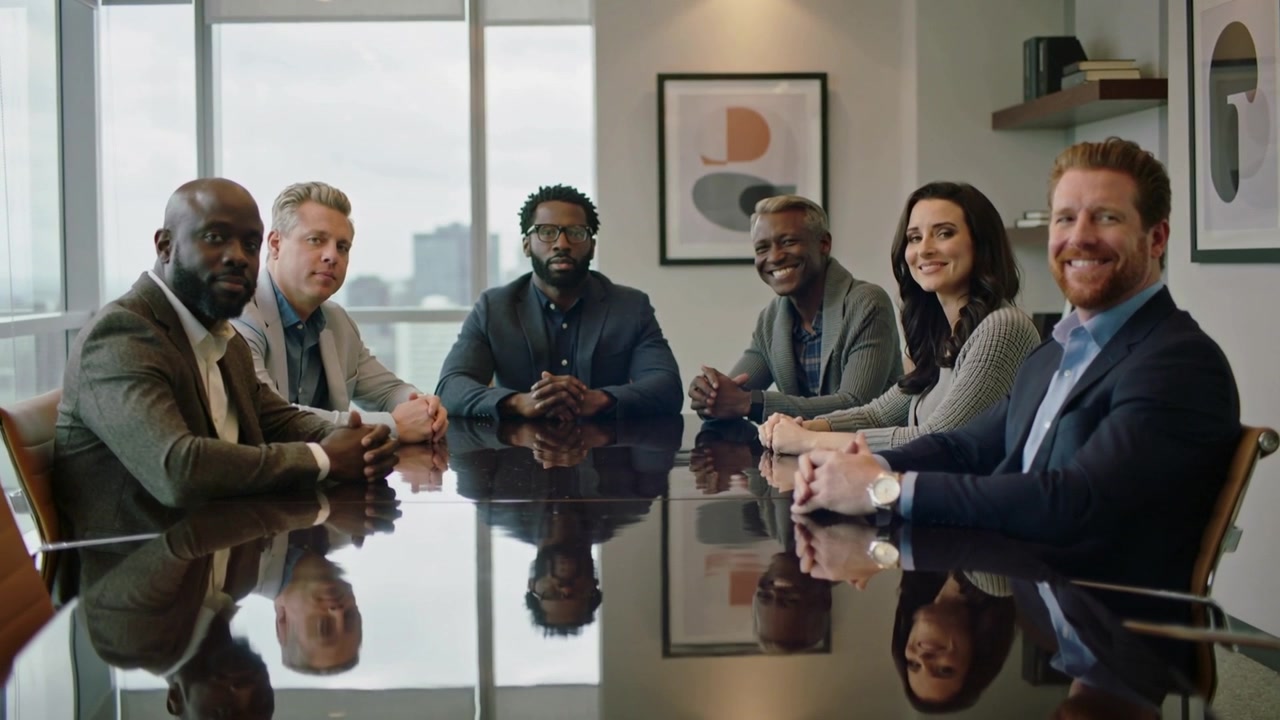 Gros plan sur six cadres en costume se détendant et souriant autour d'une table brillante dans un bureau, se mettant à l'aise.