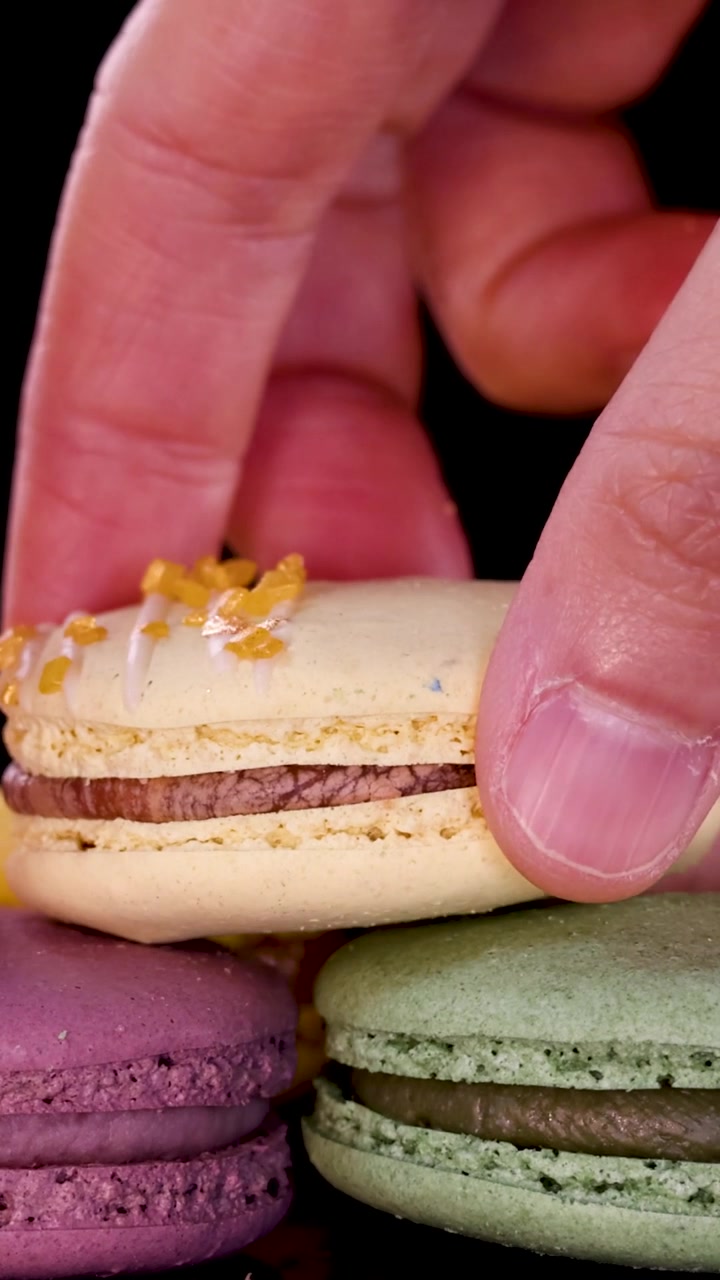 A hand reaches down to select a yellow macaron from a stack of colorful pastries.