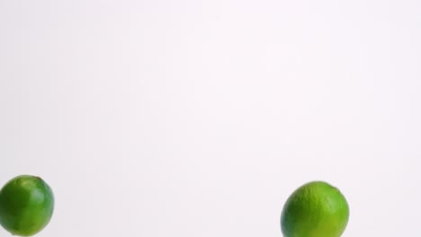 Whole-green-citrus-limes-raining-down-on-white-table-backdrop-in-slow-motion