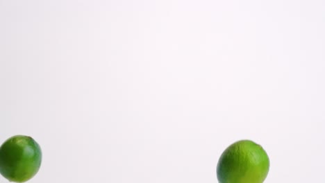 whole green citrus limes raining down on white table backdrop in slow motion