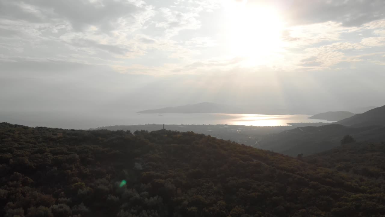 aerial  day drone shot of amazing mountain landscape  green tall trees small traditional village sun shines behind white small clouds sun reflects in the sea at background amazing view Aegean sea