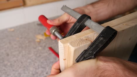 mano caucásica de un trabajador de bricolaje atornilla dos placas de madera con una abrazadera de tornillo