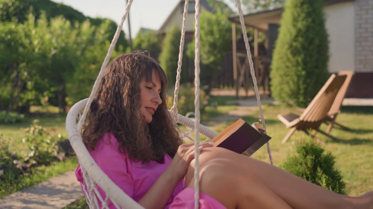 White Woman Reading In Hanging Chair Under Sun, Pink Robe And Bare Feet, Woven Wicker Swing With Rope, Pages Turning In Tranquil Backyard, Floral Borders And Calm Afternoon Solitude