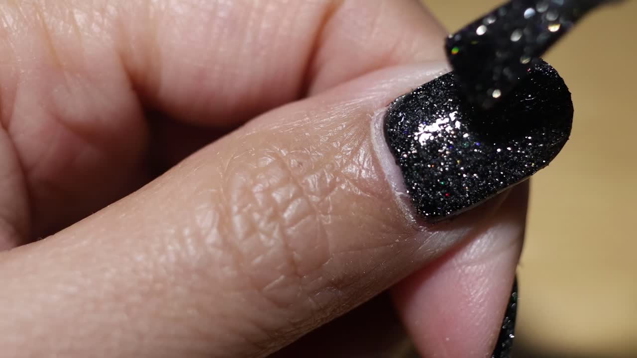 Detailed view of applying black glitter nail polish on a single fingernail.