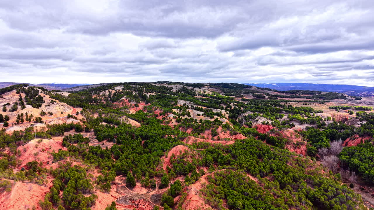 Paisaje de formaciones de suelo rojo erosionado mezclado con denso bosque de pinos verdes bajo un cielo nublado. Vista aérea de colinas de arcilla roja.