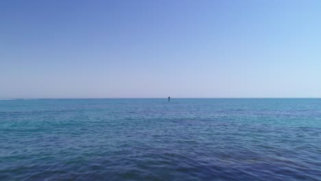 Flying-over-the-calm-waves-with-paddle-boarder-passing-by