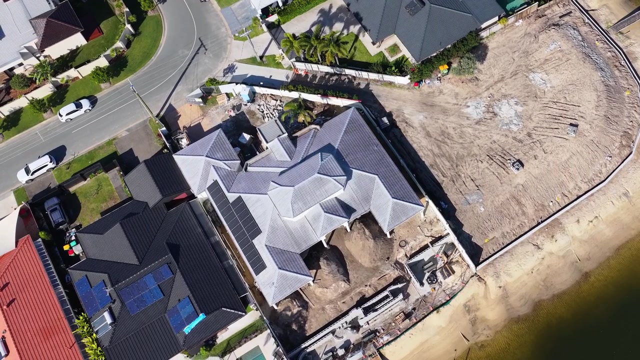 High angle drone shot reveals luxury residential construction site beside a sunny coastal canal.