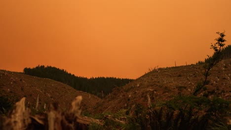Left-to-right-pan-of-orange-smoke-covered-landscape,-smoky-ridgeline-and-destroyed-trees