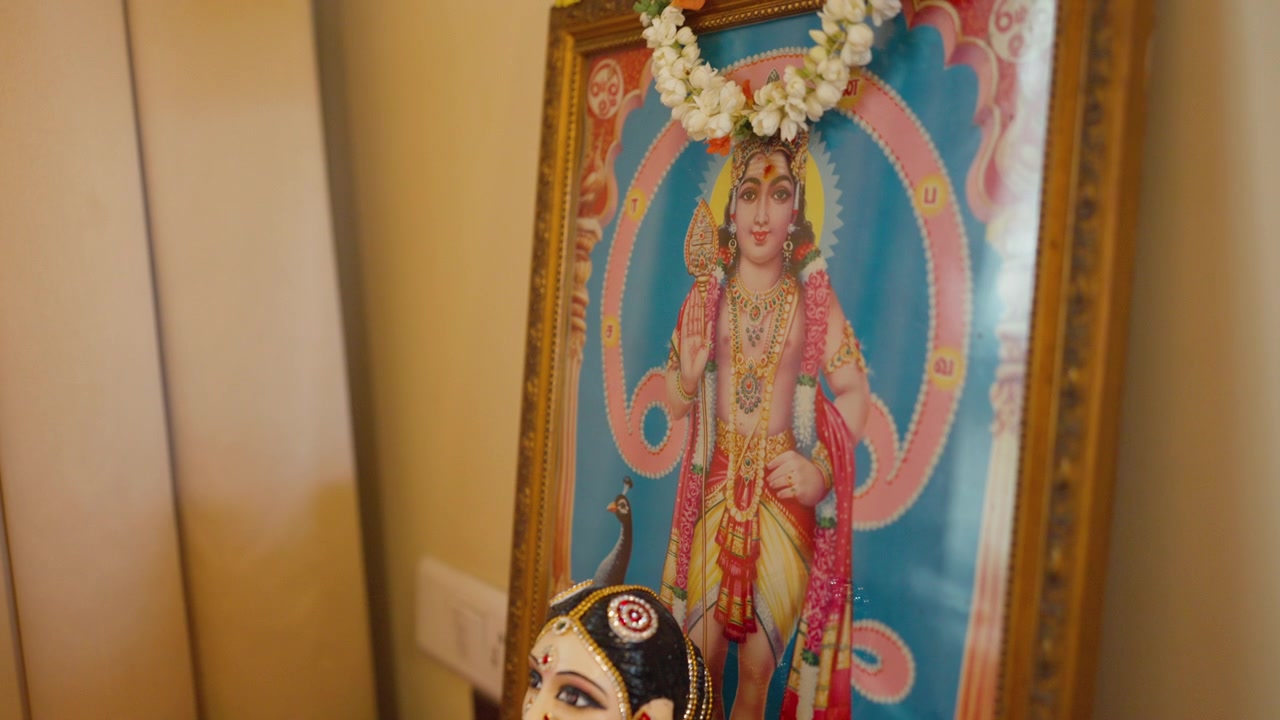 Boneca Gauri colorida do Sul da Índia sentada diante de um retrato emoldurado de uma divindade hindu decorado com uma guirlanda de flores em um casamento