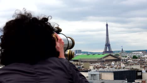 beautiful girl looking through coin operated binocular on terrace of laffaete galery in paris, france. view of eiffel tower and opera garnier at background