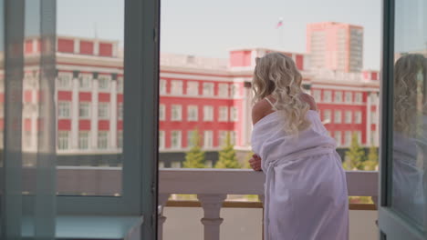 relaxed lady in sagged bathrobe leans on railing on terrace