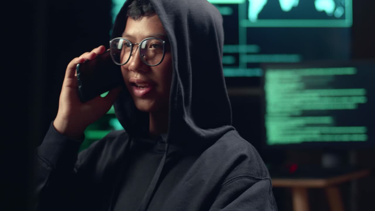 Asian Boy Hacker Using Computer Hacking And Talking On Phone