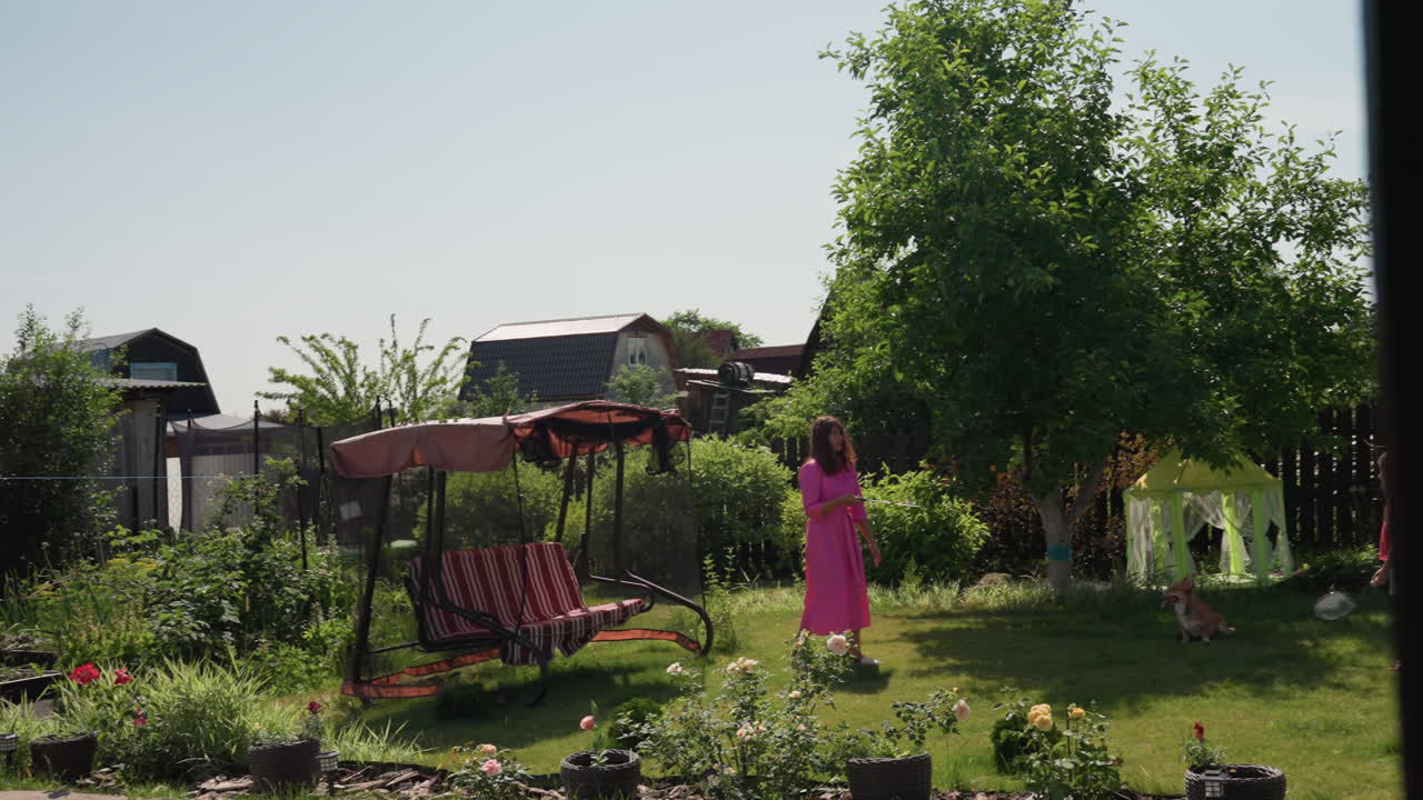 Caucasian Mother And Daughter In Garden Enjoying Sunny Backyard Play Near Swing And Playhouse, Lush Greenery, Casual Summer Dress, Joyful Waving And Gentle Bonding, Family Moment Captured