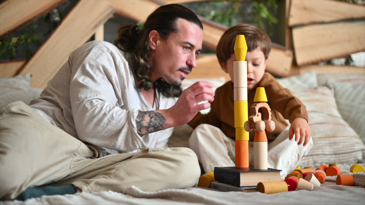 Father playing with his son with colourful, ecological wooden toys on the bed
