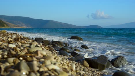 Felsen-Und-Kiesel-Am-Strand,-Der-An-Einem-Sommertag-Im-Mittelmeer-Von-Meereswellen-Auf-Einer-Wunderschönen-Meereslandschaft-Umspült-Wird