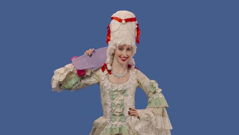 portrait of courtier lady in vintage dress and wig, holding a skateboard and showing thumbs up gesture. young woman posing in studio with blue screen background. close up. slow motion ready 59.94fps