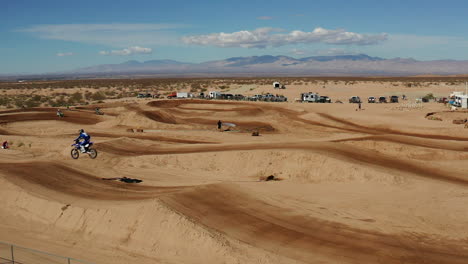 motociclista saltando de la rampa en la pista de tierra en el desierto de mojave, cámara lenta aérea