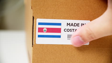 hands applying made in costa rica flag label on a shipping cardboard box with products