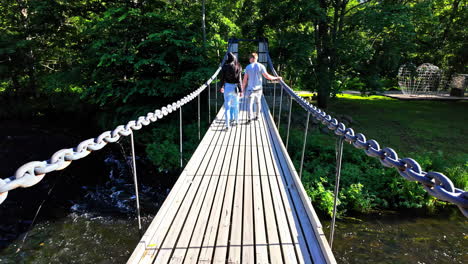 couple walking on a suspension bridge over a river in a park