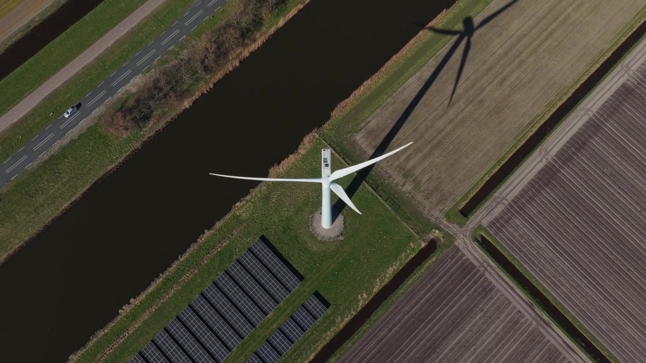 Vogelperspectief van een draaiende windturbine en aangrenzend zonnepark in een landelijk landschap, die duurzame en schone elektriciteit produceren.