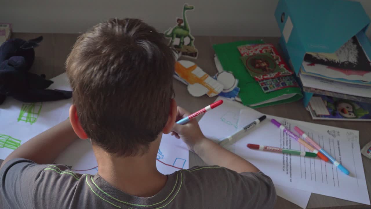 niño pequeño caucásico dibujando con marcadores de colores en el escritorio de la casa
