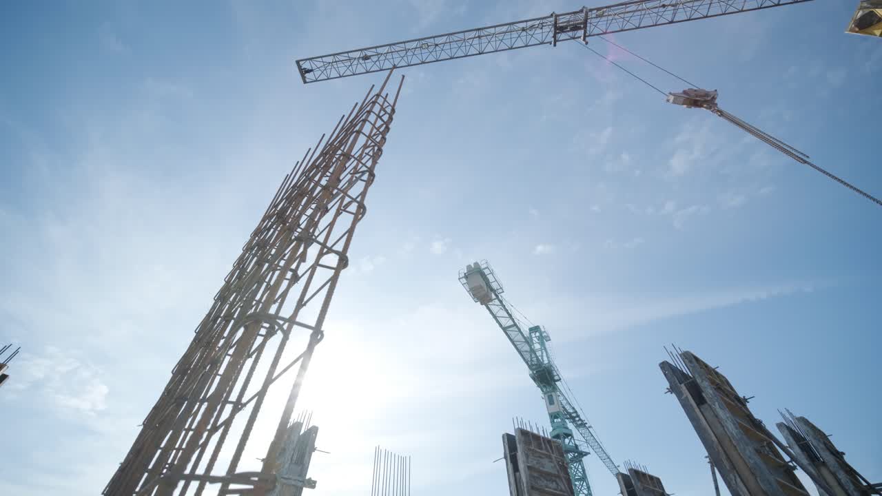 Tower cranes work on the construction of brick residential buildings against the background of a blue sky.