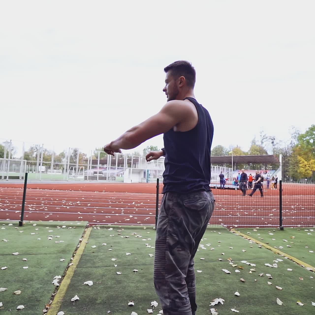 Male fitness sportsman training his body on the stadium. Muscular man dressed in black shirt exercises on autumn background. Slow motion. Healthy lifestyle.