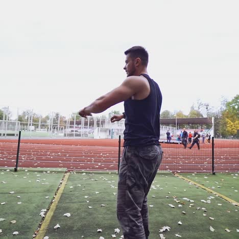 male fitness sportsman training his body on the stadium. muscular man dressed in black shirt exercises on autumn background. slow motion. healthy lifestyle.