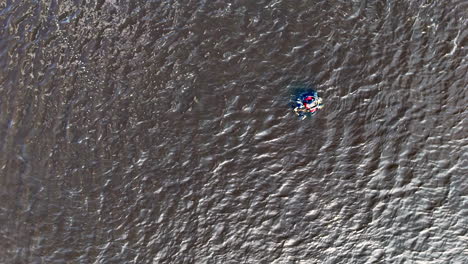 Scuba diver wearing full equipment with visible red and blue accents floats on the surface of rippling water, surrounded by textured waves reflecting shifting light