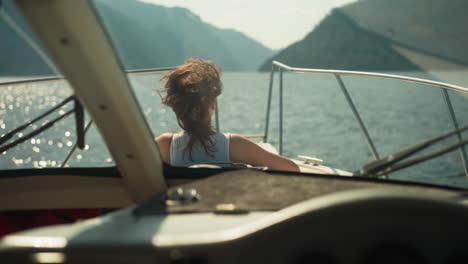 curious female enjoys picturesque views from yacht sailing rolling mountains in sunny weather. spending time in nature and leisure activity