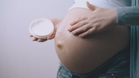 pregnant lady applies cream on belly at white wall closeup