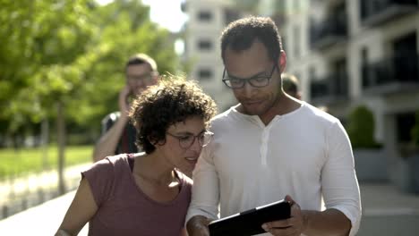 pareja sonriente con gafas sosteniendo dispositivos en la calle