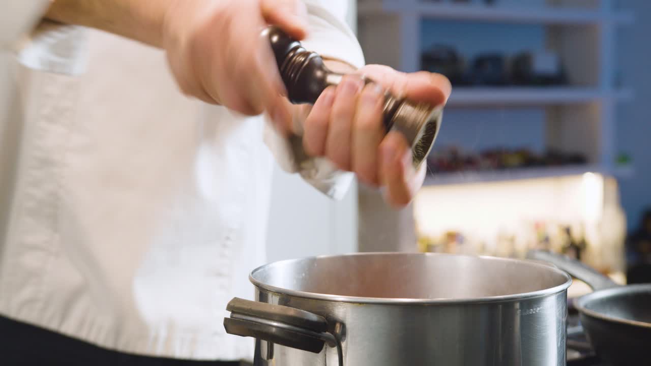 Chef grinds pepper in steaming pot. Handheld shot
