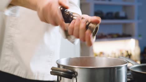 chef grinds pepper in steaming pot. handheld shot