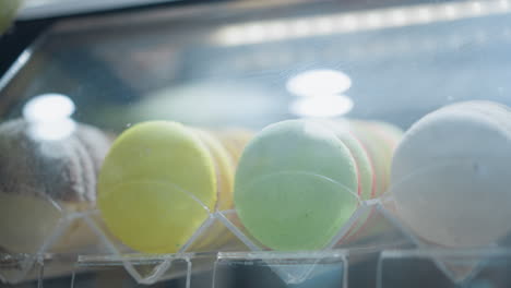 close-up of assorted colorful macarons arranged in a display case with light reflecting on glass, showcasing yellow, green, and white macarons