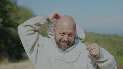 a beekeeper removes his protective hood outdoors