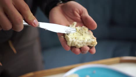 Hombre-Caucásico-Unta-Mantequilla-En-Un-Bollo-Tradicional-De-Nueva-Zelanda-Recién-Horneado