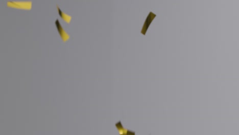 Stationary-Shot-of-Gold-and-White-Confetti-Falling-Against-a-Grey-Background