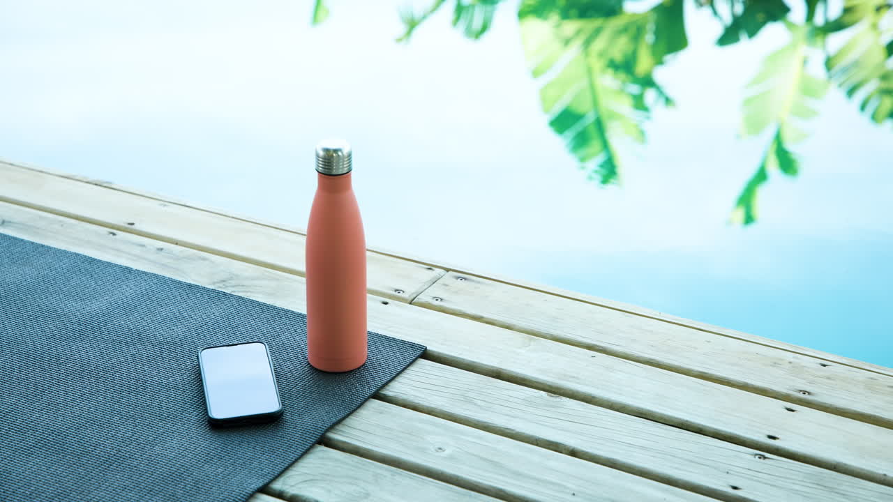 Yoga mat, smartphone, and water bottle by poolside, relaxing outdoors, copy space