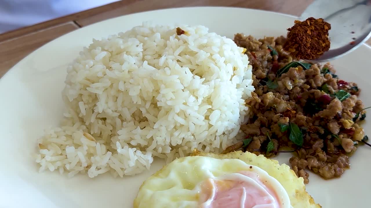 A plate with rice, stir-fried meat, and a fried egg being garnished with spices.