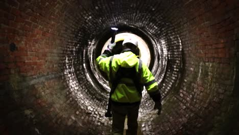 Un-Trabajador-Del-Distrito-De-Alcantarillado-Conduce-El-Camino-Con-Una-Luz-Por-Un-Antiguo-Túnel-De-Alcantarillado-Del-Siglo-XIX