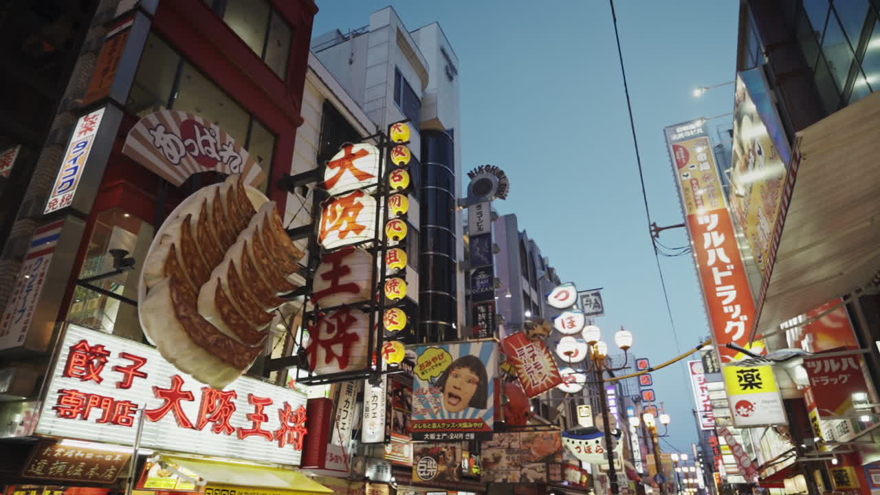 Dotonbori signage illuminated at dusk, Osaka, Japan, wide pan right in slow motion.