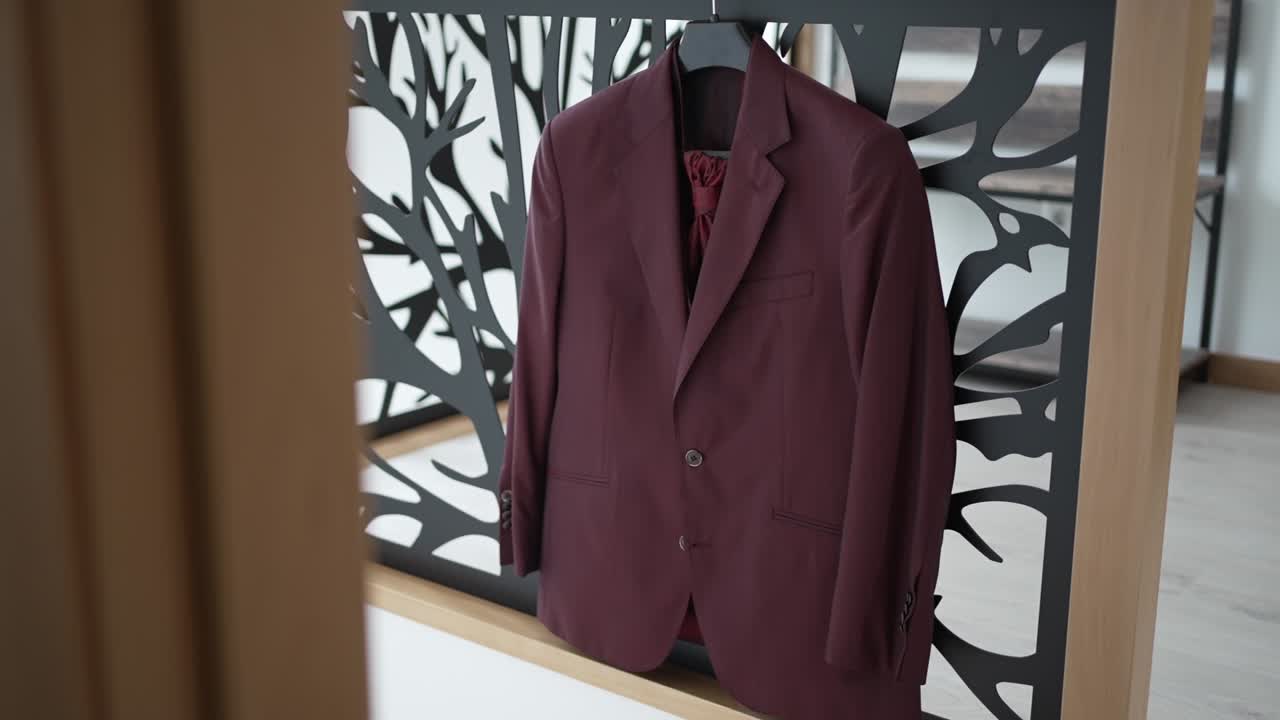 Burgundy groom suit with matching cravat hanging on a decorative frame